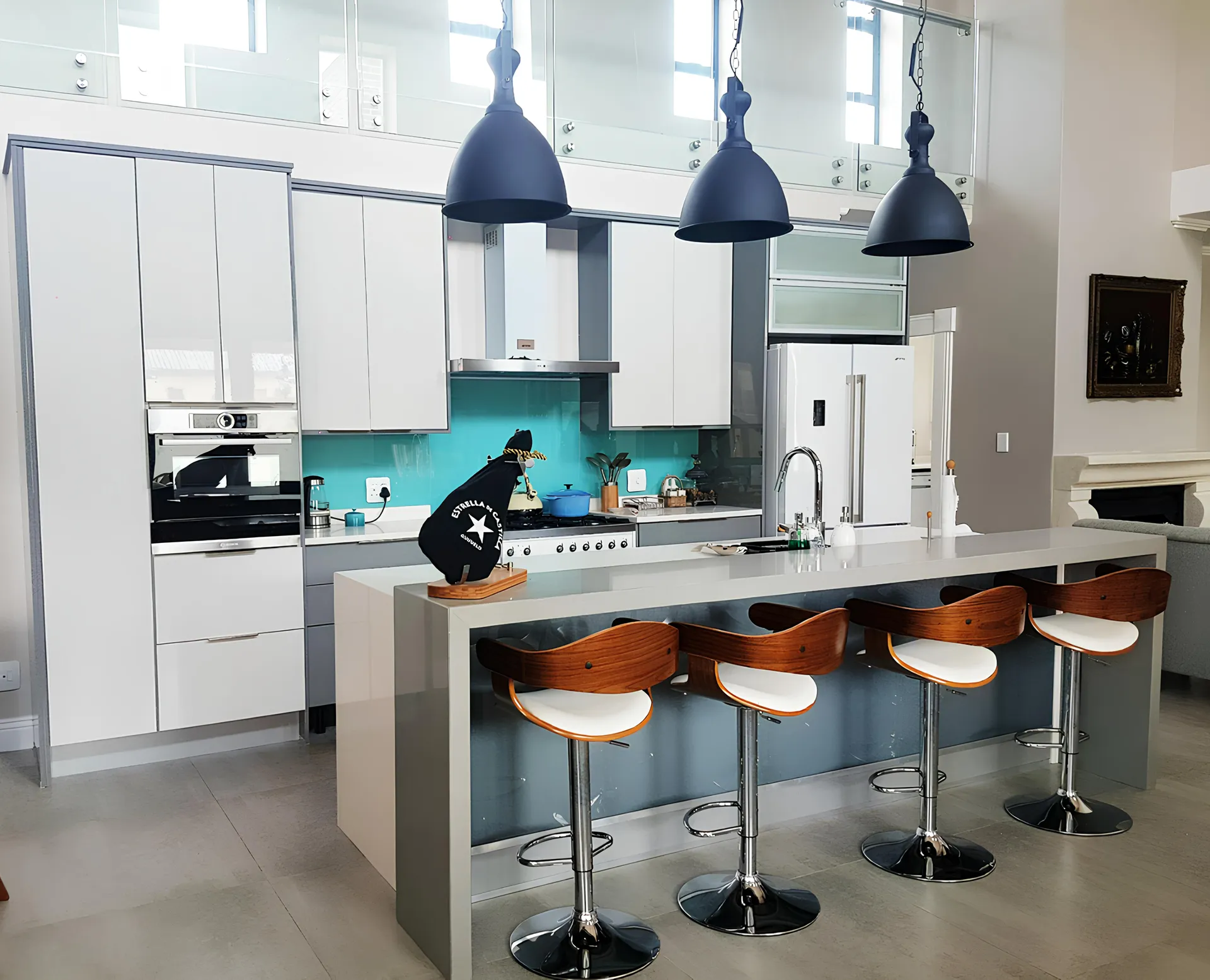Double-volume kitchen with a teal glass splashback and island seating, fitted by N.D.I.